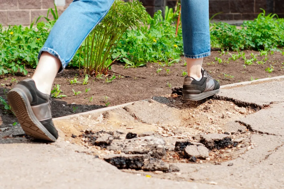 Person stepping over hole in sidewalk.